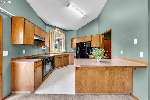 kitchen featuring light countertops, under cabinet range hood, black appliances, vaulted ceiling, and a peninsula