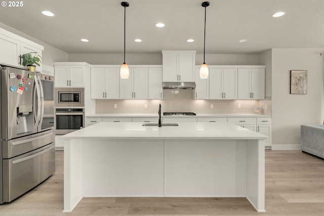 kitchen with decorative light fixtures, sink, appliances with stainless steel finishes, and a center island with sink