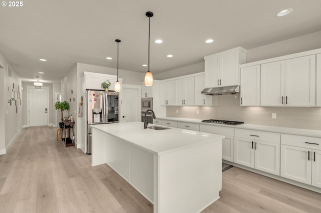 kitchen with white cabinets, appliances with stainless steel finishes, sink, backsplash, and a center island with sink