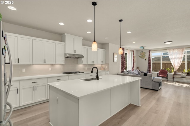 kitchen featuring decorative light fixtures, white cabinetry, stainless steel appliances, an island with sink, and sink