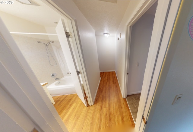 hallway with light hardwood / wood-style floors and a textured ceiling