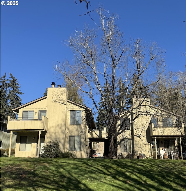 rear view of property featuring a lawn, a chimney, and a balcony