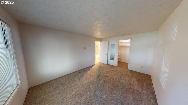 unfurnished bedroom with a closet, carpet flooring, a textured ceiling, and a spacious closet