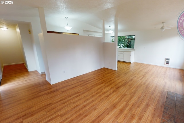 interior space with heating unit, vaulted ceiling, a textured ceiling, light wood-type flooring, and ceiling fan