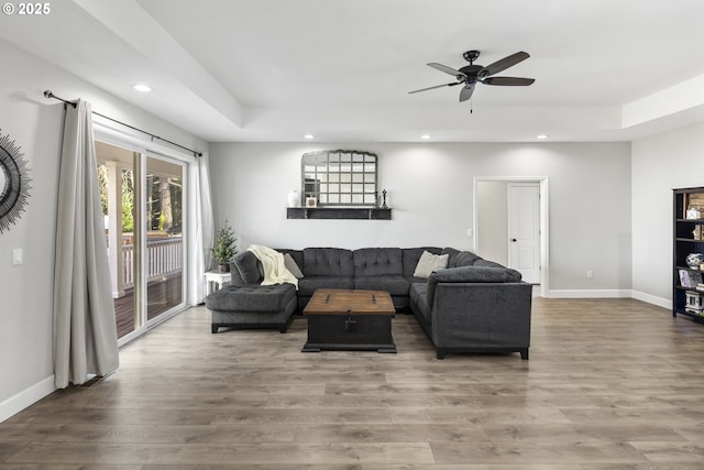 living room with wood-type flooring, a raised ceiling, and ceiling fan