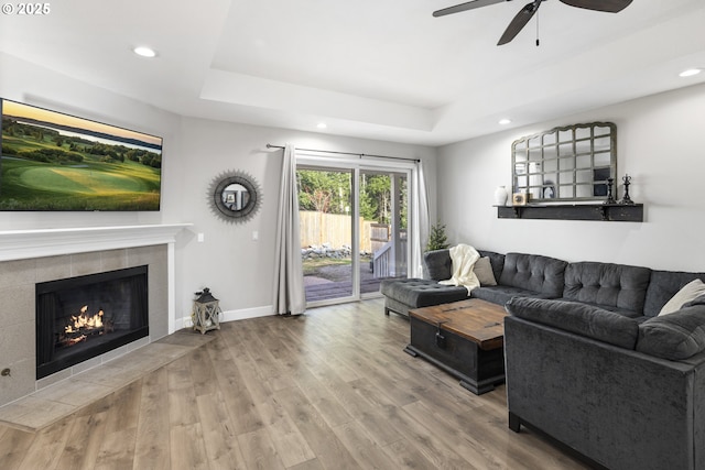 living room featuring a tiled fireplace, a raised ceiling, hardwood / wood-style floors, and ceiling fan