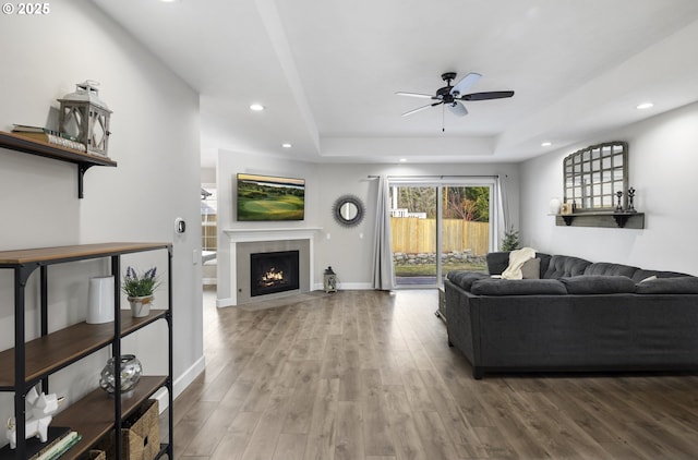 living room with hardwood / wood-style floors, a tray ceiling, and ceiling fan