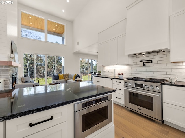 kitchen featuring light hardwood / wood-style flooring, white cabinetry, a towering ceiling, stainless steel appliances, and a stone fireplace