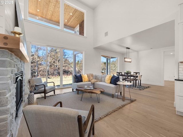 living room featuring a high ceiling, a stone fireplace, wooden ceiling, and light hardwood / wood-style flooring