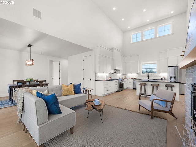 living room featuring a towering ceiling, sink, a fireplace, and light wood-type flooring