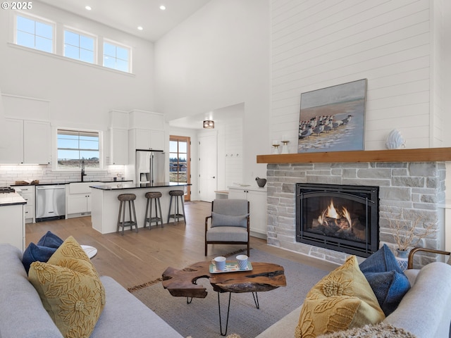 living room featuring a high ceiling, a stone fireplace, sink, and light hardwood / wood-style floors