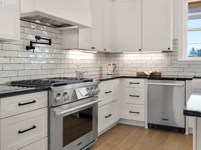 kitchen featuring dark stone countertops, white cabinets, stainless steel appliances, custom range hood, and light hardwood / wood-style flooring