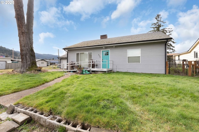 rear view of house with a chimney, fence, and a lawn