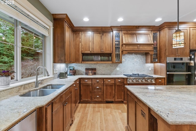 10137 SW Lancaster Rd, Portland, OR 97219 - kitchen featuring appliances with stainless steel finishes, light wood-style floors, brown cabinetry, light stone counters, and premium range hood