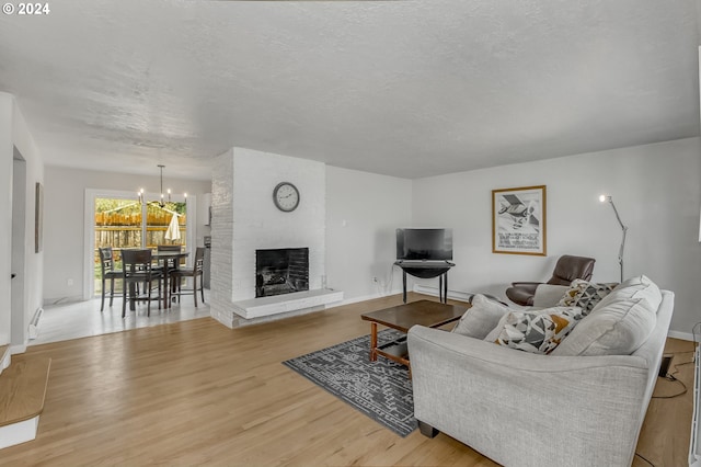 living room with a textured ceiling, light hardwood / wood-style floors, a brick fireplace, and a notable chandelier