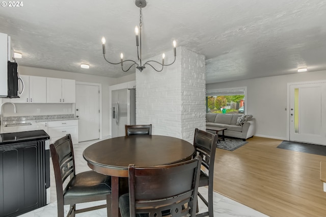 dining space with a notable chandelier, light hardwood / wood-style floors, sink, and a textured ceiling