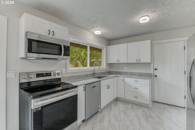 kitchen with sink, stainless steel appliances, light stone counters, a textured ceiling, and white cabinets