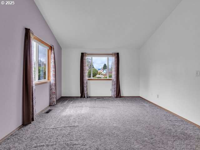 carpeted empty room featuring baseboards, vaulted ceiling, and visible vents