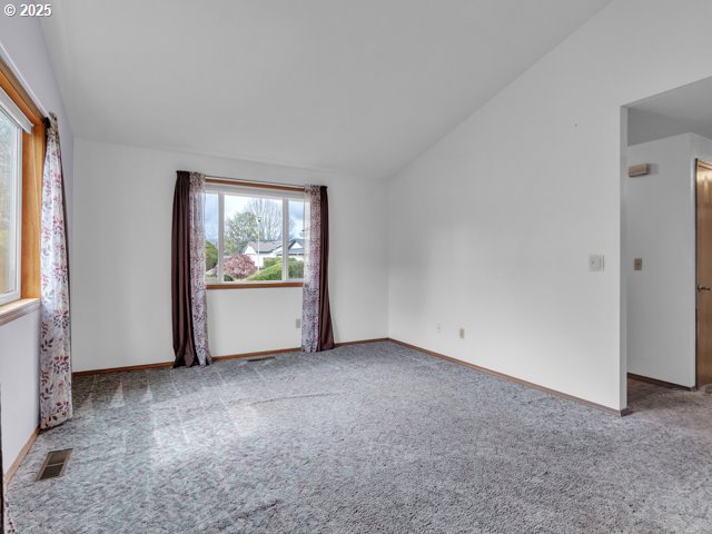 empty room with carpet flooring, baseboards, lofted ceiling, and visible vents