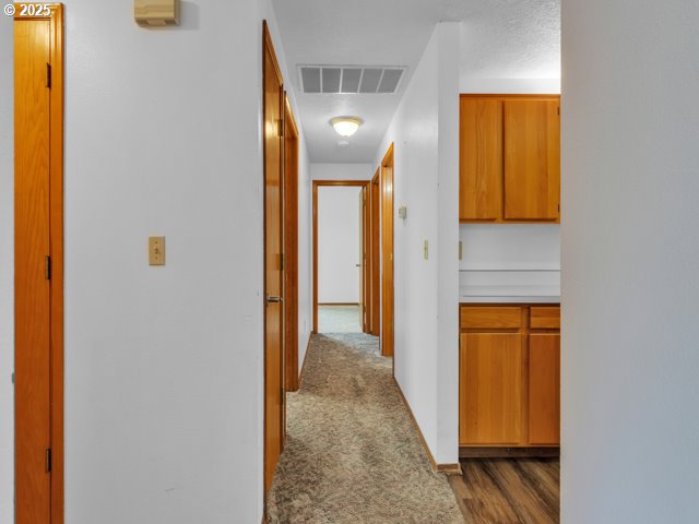 hall featuring baseboards, dark colored carpet, and visible vents