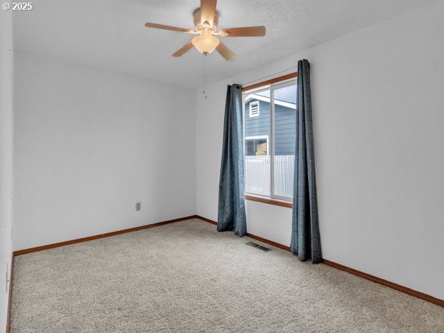 carpeted spare room with visible vents, baseboards, and ceiling fan