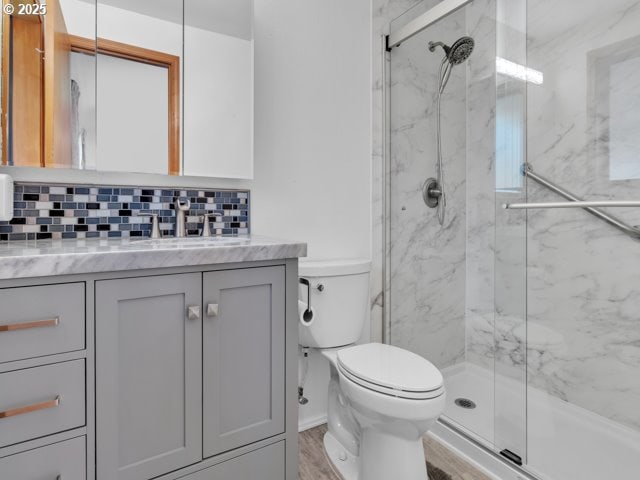 bathroom with decorative backsplash, a marble finish shower, toilet, and vanity