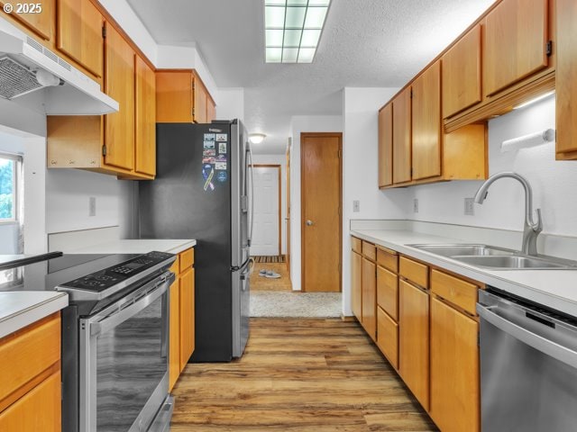 kitchen featuring light countertops, a sink, light wood-type flooring, under cabinet range hood, and stainless steel appliances
