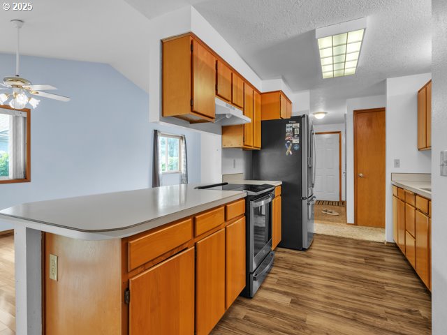 kitchen featuring stainless steel appliances, under cabinet range hood, ceiling fan, a peninsula, and wood finished floors