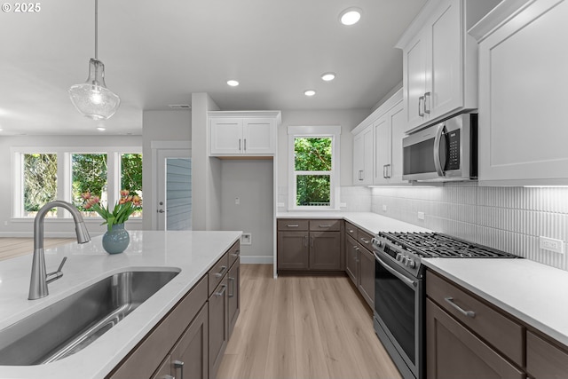 16401 SW Cambridge Ln, Durham, OR 97224 - kitchen featuring stainless steel appliances, a sink, light wood-style floors, white cabinetry, and decorative backsplash