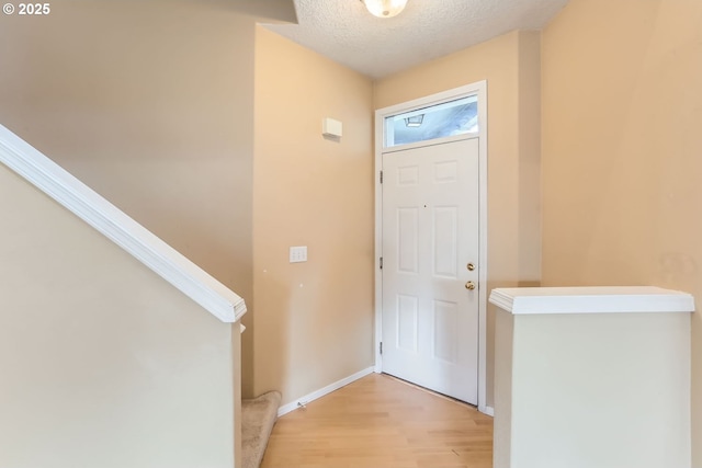 foyer with light wood-style floors, baseboards, stairway, and a textured ceiling