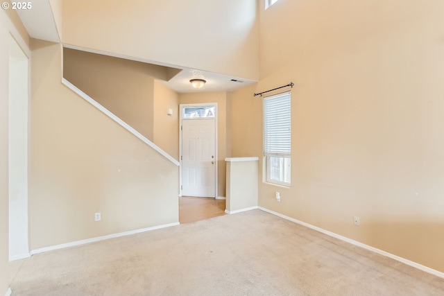 entryway featuring a high ceiling, light carpet, plenty of natural light, and baseboards