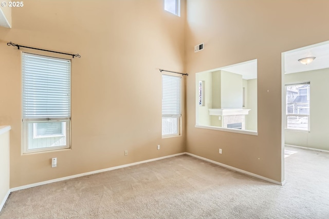 empty room with visible vents, a high ceiling, light carpet, a tile fireplace, and baseboards