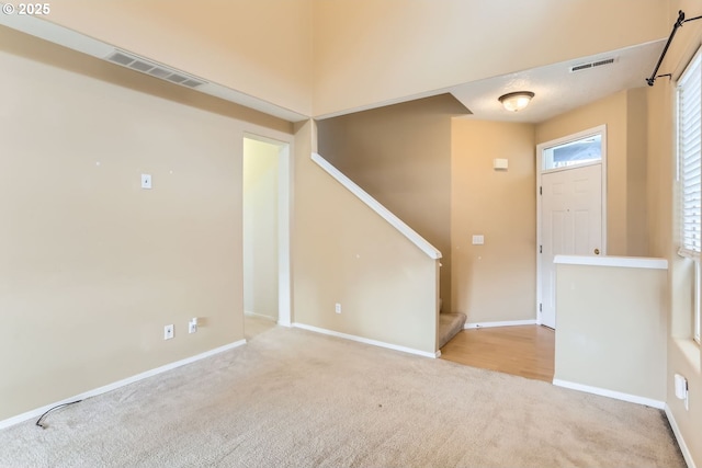 entrance foyer with baseboards, stairs, visible vents, and light colored carpet