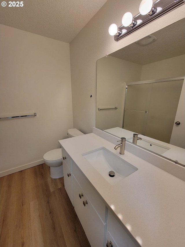 bathroom with hardwood / wood-style floors, a shower with shower door, vanity, toilet, and a textured ceiling