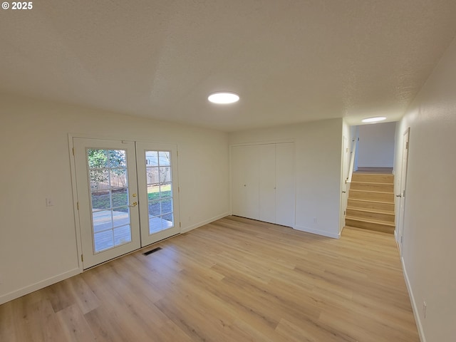 empty room featuring light hardwood / wood-style floors, french doors, and a textured ceiling