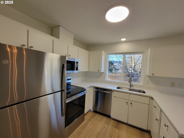 kitchen with stainless steel appliances, sink, light hardwood / wood-style flooring, and white cabinets