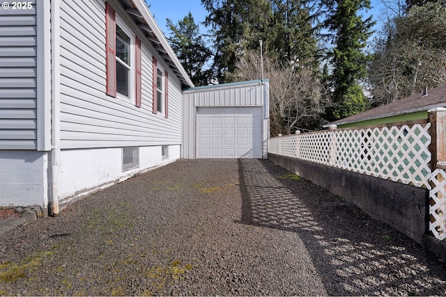 view of side of home featuring driveway, a detached garage, fence, and an outdoor structure