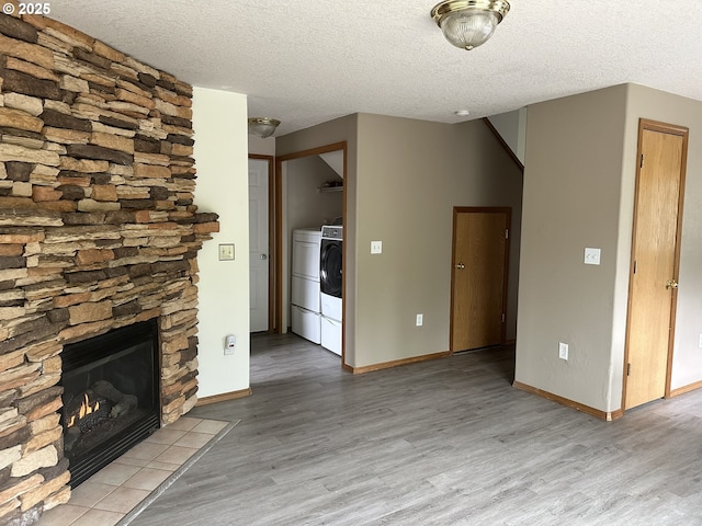 14237 SE Lee Ave, Milwaukie, OR 97267 - unfurnished living room with light wood-style flooring, a textured ceiling, a stone fireplace, baseboards, and washer and dryer