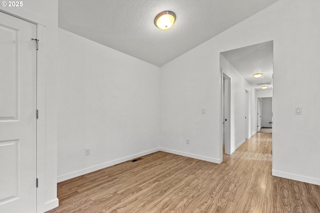 unfurnished room featuring light hardwood / wood-style flooring, a textured ceiling, and lofted ceiling