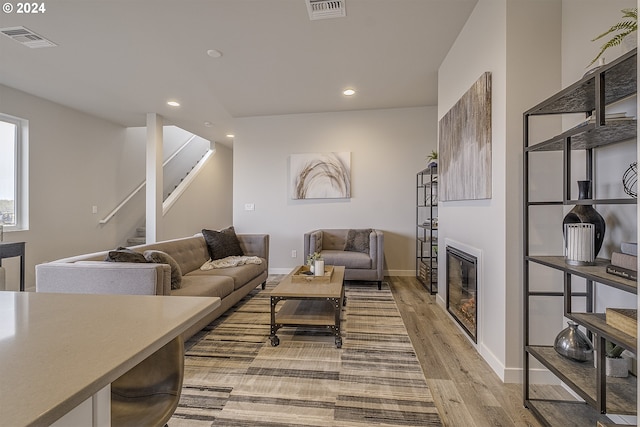 living room with light wood-type flooring, a glass covered fireplace, visible vents, and recessed lighting