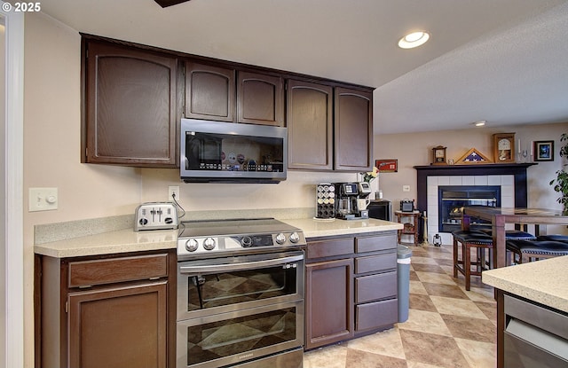 kitchen featuring stainless steel appliances, a fireplace, and dark brown cabinetry