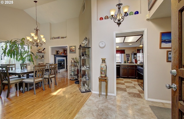 dining area with light wood-type flooring, a tile fireplace, lofted ceiling, and an inviting chandelier