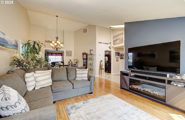 living room featuring high vaulted ceiling, a chandelier, and light hardwood / wood-style flooring