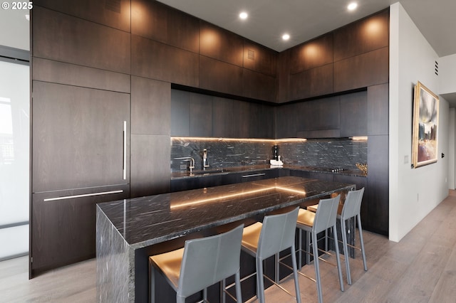 kitchen featuring sink, a breakfast bar area, light hardwood / wood-style flooring, a kitchen island, and decorative backsplash