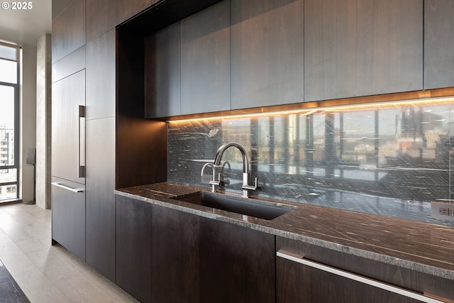 kitchen featuring tasteful backsplash, dark stone counters, light hardwood / wood-style floors, and sink