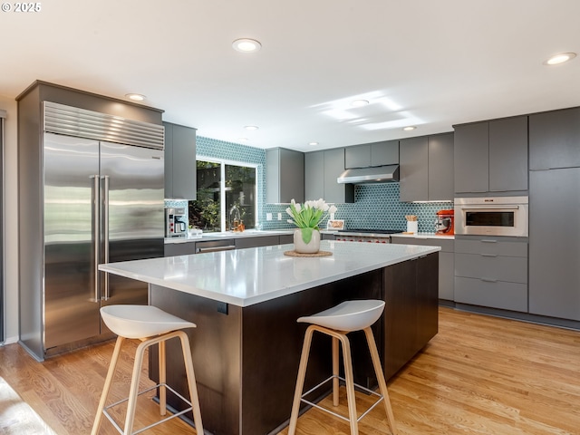 2490 SW Scenic Dr, Portland, OR 97225 - kitchen with appliances with stainless steel finishes, under cabinet range hood, a kitchen bar, modern cabinets, and recessed lighting