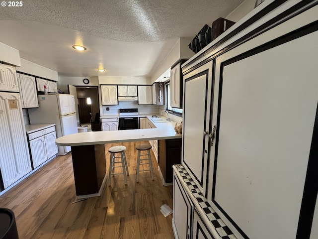 kitchen with electric range, a sink, wood finished floors, a peninsula, and exhaust hood