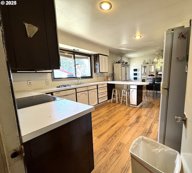 kitchen with light countertops, light wood-style flooring, a textured ceiling, white appliances, and a peninsula