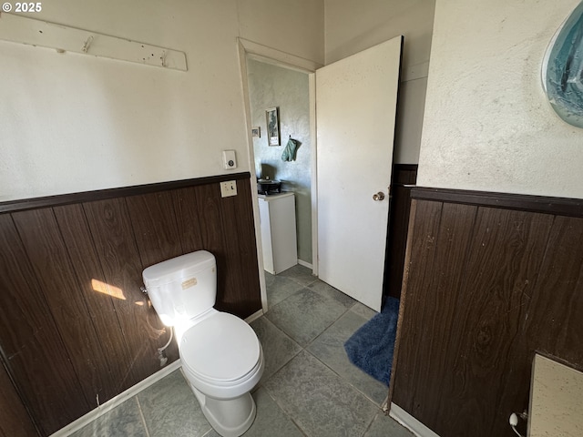 bathroom featuring wainscoting, wooden walls, toilet, and tile patterned floors