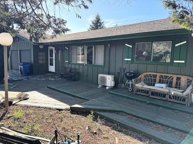 rear view of house featuring roof with shingles, board and batten siding, a wooden deck, and ac unit